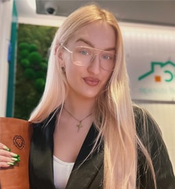 A woman with long blonde hair and blue eyes. She wears glasses and a black blazer. Attic Self Storage is on the background.
