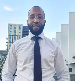 A man with a black beard smiles at the camera. He wears a formal white shirt and black tie.