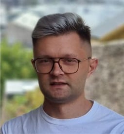 A selfie of a man smiling at the camera. He has bleached silver hair and wears glasses.