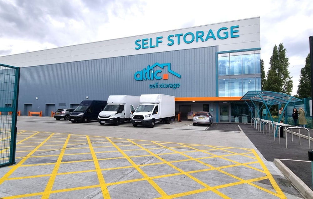 A self storage facility with trucks parked in front. The storage building has a grey brick exterior and a metal roof.