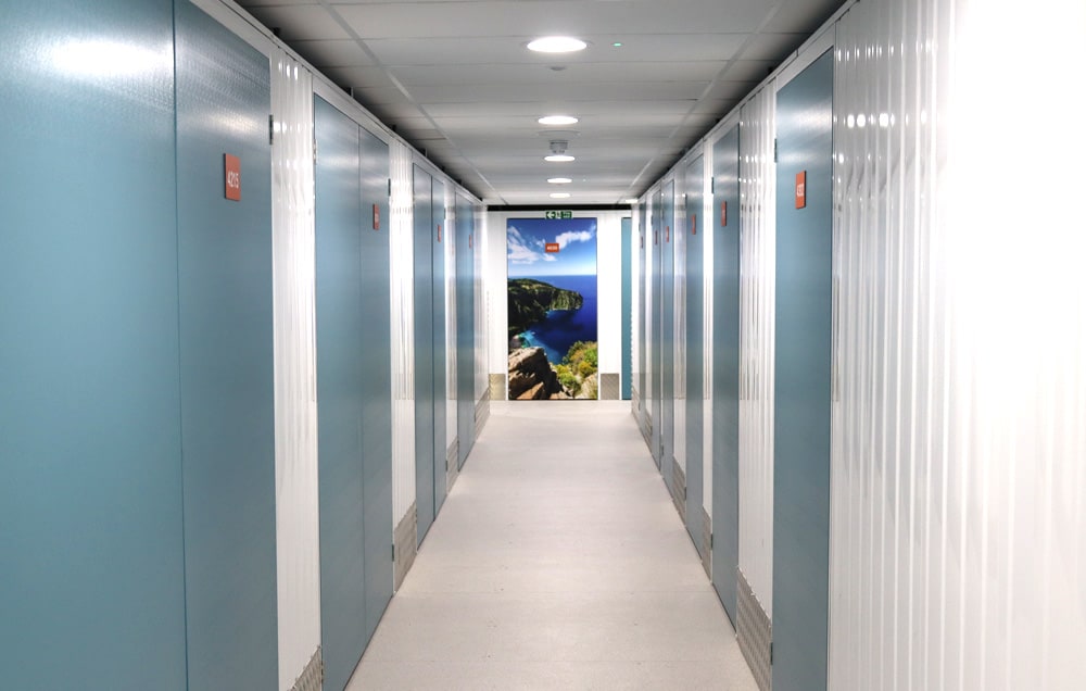 A long hallway of storage facility with lockers and a door with a picture of a beach on the wall.