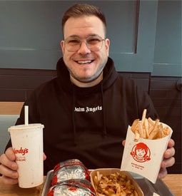 Man in black hoodie and glasses enjoys fries and Coke at a fast food restaurant.