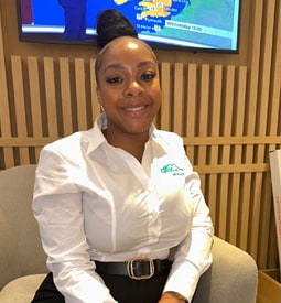 Attic Self Storage employee, a woman of colour, smiles at the camera dressed in a white button-down shirt with company logo.